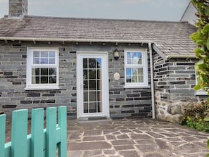 A stone cottage with a tiled roof, a white door, and a small window with a lantern. - Ty Llaeth Cottage, Tywyn (Tywyn)