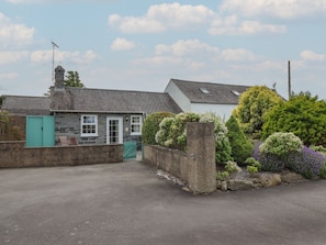 A stone building with a tiled roof, a green door, and a fenced yard with various plants. - Ty Llaeth Cottage, Tywyn (Tywyn)