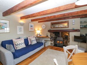 Ein gem ütliches Wohnzimmer mit Kamin aus Stein, Holzbalken, einem blauen Sofa und einem weißen Esstisch.