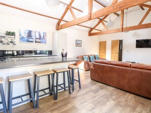 Eine moderne Küche mit Barbereich, einem braunen Ledersofa und Holzbalken an der Decke.