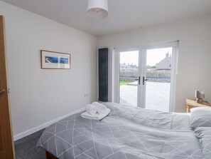 Ein Schlafzimmer mit einem Bett, einem gerahmten Bild, einer Tür und Blick durch eine Glasdoor.