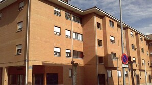 Un immeuble en briques de plusieurs étages, doté d’un toit plat, de nombreuses fenêtres et d’un panneau indiquant qu’il est interdit de se garer.