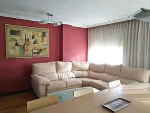 Ein Wohnzimmer mit einem beigefarbenen Ecksofa, einem Glastisch, einer roten Akzentwand und einem großen abstrakten Gemälde.
