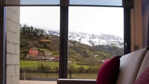 Une pièce dotée d’une grande fenêtre donnant sur un paysage montagneux, avec des sommets enneigés et un bâtiment rouge visible au loin.