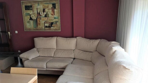 Un salon avec un canapé d’angle beige, une petite table et un tableau accroché au mur.
