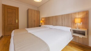 Une chambre à coucher avec un grand lit, une tête de lit en bois, deux tables de chevet avec des lampes et une armoire en bois.