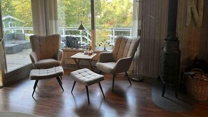 Una habitación acogedora con chimenea, dos sillones, una mesa y vistas a una terraza y árboles.
