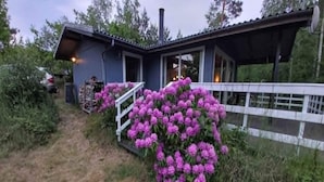 Una casa con un porche, un jardín de flores moradas y una cerca blanca.
