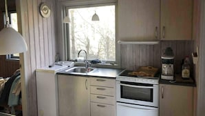 Una cocina compacta con pileta, estufa y horno, paredes de madera y una ventana con vista a árboles.