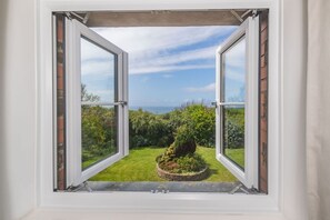 Une fenêtre ouverte donnant sur un jardin et un paysage lointain.