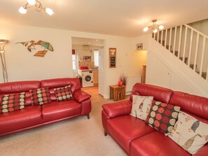 A living room with two red leather sofas, a staircase, and a kitchen in the background. - White Goose Cottage, Whitby (Whitby)