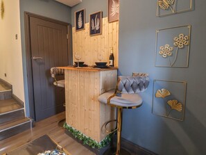 Un coin bar en bois avec un tabouret rembourré, une bouteille de vin et des œuvres d’art encadrées accrochées au mur.