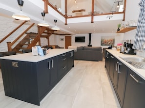 A modern kitchen with a central island, dark cabinetry, and a staircase leading to an upper level. - Merddwr, Cerrigydrudion (Corwen)