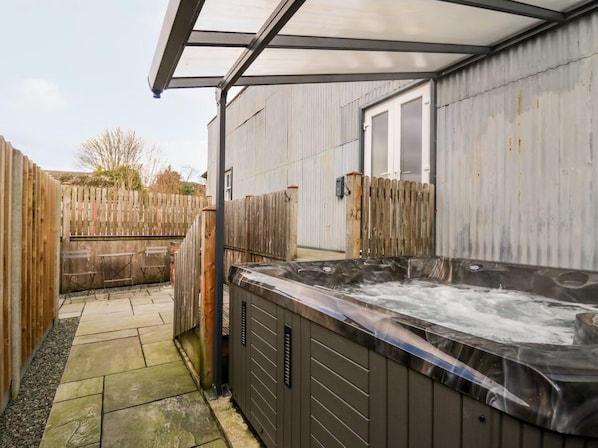 A hot tub in a covered outdoor area with a wooden fence and a metal building in the background.