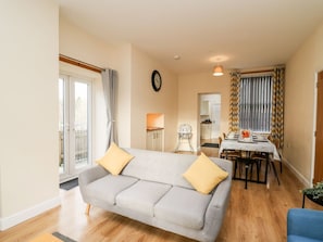 A living room with a sofa, dining table, and kitchen in the background.