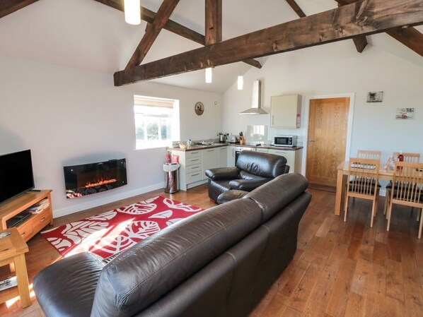 A living room with a leather sofa, wooden dining table, and chairs, a kitchen with white cabinets, and a fireplace.
