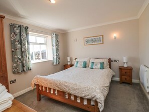 A bedroom with a bed, two bedside tables, a window with curtains, a wall-mounted light, and a radiator. - Freeborough, Moorsholm (Saltburn-by-the-Sea)