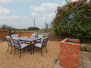 An outdoor patio with a table and chairs, a brick barbecue, and a wooden fence. - 6 Gravel Hill, Burnham Market (King's Lynn)