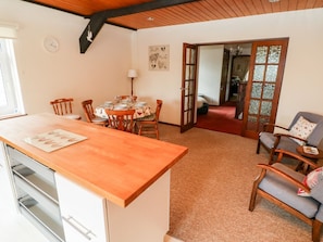 A dining area with a wooden table and chairs, a kitchen with a wooden countertop, and a living area with a sofa and armchairs.