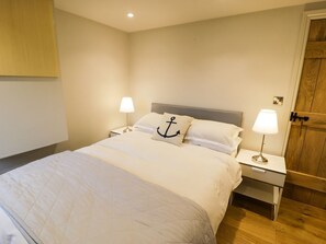 Une chambre à coucher comprenant un lit, deux lampes de chevet, une table de chevet, une porte en bois et un luminaire fixé au mur.