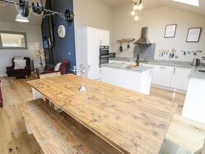 A modern kitchen with a central island, white cabinetry, and a dining area with a wooden table and benches.