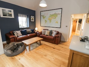 A living room with a brown leather sectional sofa, a wooden coffee table, a gray bean bag, a world map on the wall, and a window with blinds.