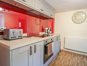 Eine moderne Küche mit grauen Schränken, einer roten Spritzschutzwand, einem eingebauten Backofen und einer Wanduhr.