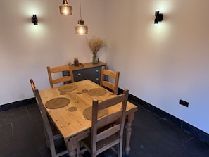 Una mesa de madera con cuatro sillas, un florero con flores secas e iluminación colgante.