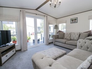 Una sala de estar con sofá, reposapiés, televisor y puerta corrediza de vidrio que da a un área exterior.