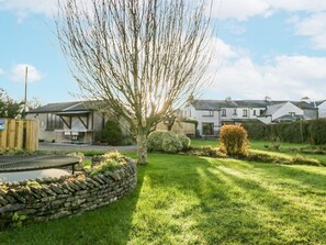 A residential area with a stone wall, a tree, and houses in the background. - 1 Gilpin House, Levens Cumbria (Kendal)