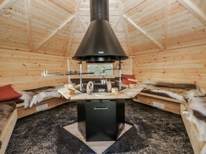 A log cabin interior with a central wood stove, wooden walls, and fur-lined benches. - 1 Gilpin House, Levens Cumbria (Kendal)