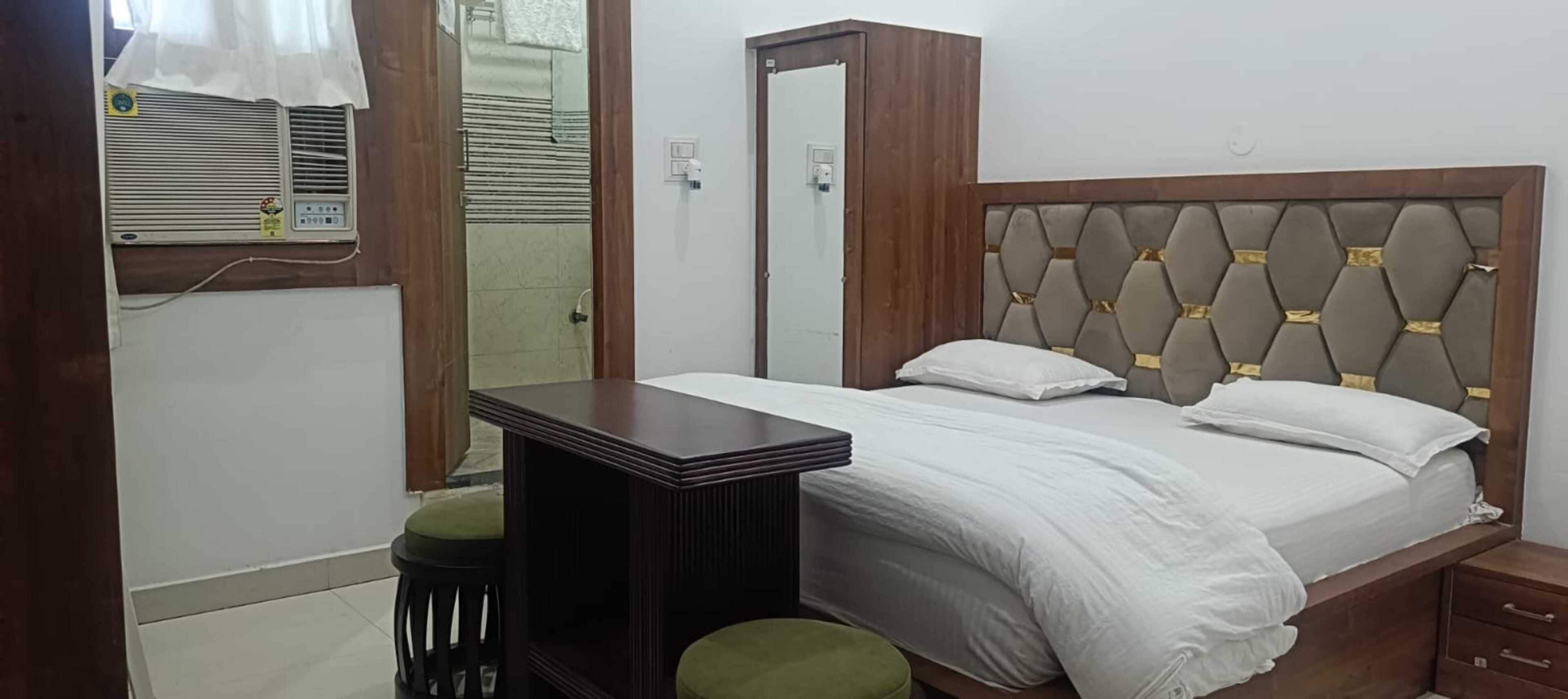A bedroom with a bed, a bedside table, a mirror, a heater, and a small stool.