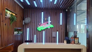 Un comptoir d’accueil avec un mur revêtu de panneaux en bois, un panneau néon indiquant « Restaurant Sagar » et un ventilateur fixé au mur.