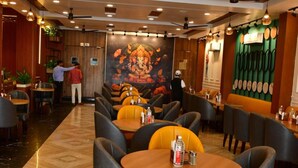 Un restaurant avec des tables rondes, des chaises grises, des ventilateurs de plafond et une fresque murale.