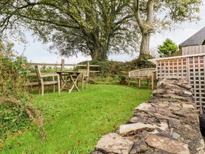 Un mur de pierres, une clôture en bois et un grand arbre dans un jardin.