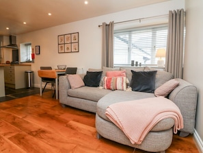 A living room with a sofa, a dining table, and a kitchen area.