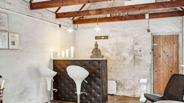 Ein Zimmer mit einem gepolsterten Kopfteil, einer Buddha-Statue, einem weißen Stuhl, einem Korbstuhl und einem gefliesten Boden.
