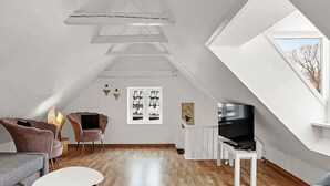 Ein modernes Loft mit schrägverdeckter Decke, einem Flachbildfernseher, einem Kamin und einem großen Fenster.