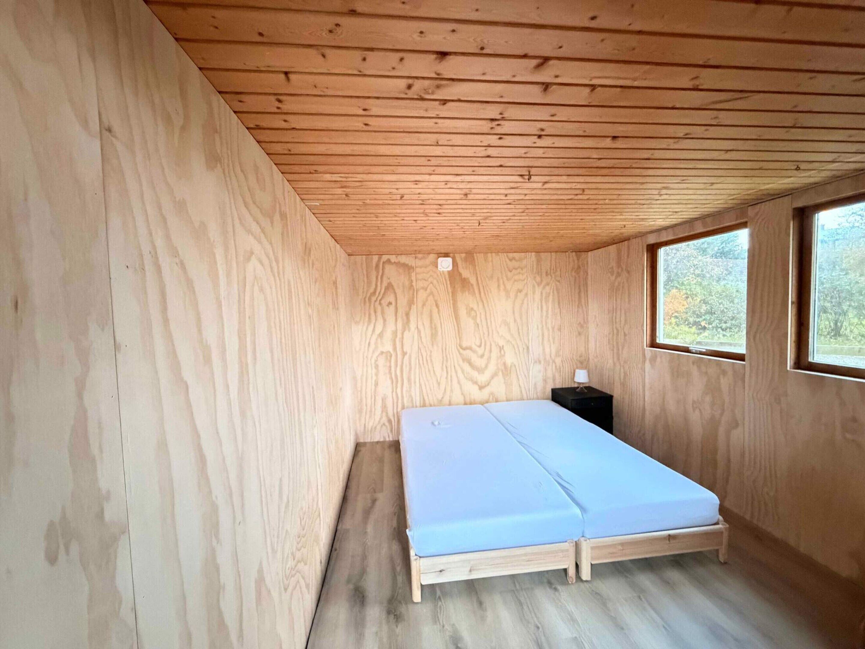 Ein kleines Zimmer mit Holzboden, einem Bett, einem Nachttisch und einem Fenster.