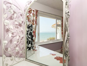 Ein Zimmer mit einem großen Spiegel, der einen Blick auf das Meer, eine weiße Tür und eine rosa Wand reflektiert.