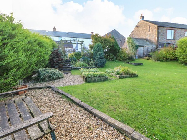 A garden with a wooden bench, a stone wall, and a building with a pitched roof.