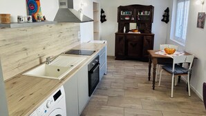 A compact kitchen with a built-in washing machine, a dining area with a table and chairs, and a dark wooden cabinet. - Charming 1-bedroom house in Azille perfect for a relaxing getaway (Azille)