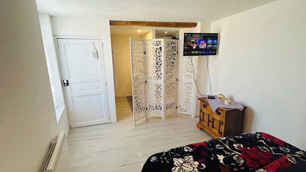 A hotel room with a bed, a TV, a wooden cabinet, a decorative screen, and a white door. - Charming 1-bedroom house in Azille perfect for a relaxing getaway (Azille)