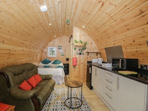 Ein gemütliches Blockhaus-Interieur mit Holzbalkendecke, einem Bett mit Kissen, einer Couch, einem kleinen runden Tisch und einer Küchenzeile mit Mikrowelle.