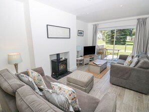 A living room with a fireplace, sofas, a TV, and a view of a garden.