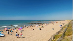 Een strand met mensen, parasols en een houten omheining.