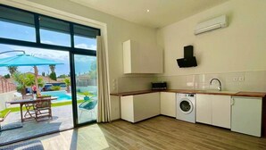 Een moderne keuken met een ingebouwde wasmachine, een grote schuifpui naar een zwembad en een eethoek met tuinmeubilair.