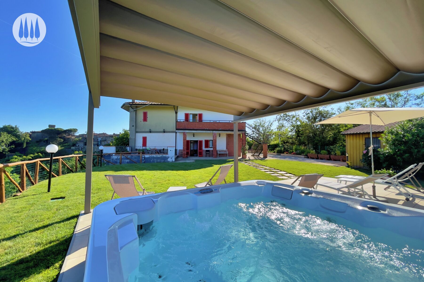 A covered outdoor area with a hot tub, a pool, and a view of a two-story house with red shutters.