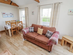 A cozy room with a brown sofa, plaid cushions, a wooden dining table, and a window with curtains. - Home Stead Cottage, Embleton (Alnwick)