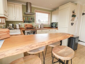 Una cocina con una isla de madera, taburetes de bar, estufa y una ventana con persianas.